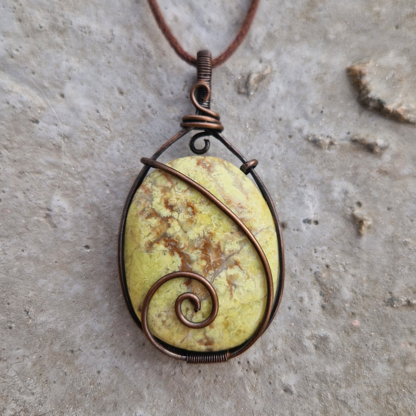 A close-up of a Green Opal wire wrapped pendant on a wax cord, for healing from grief