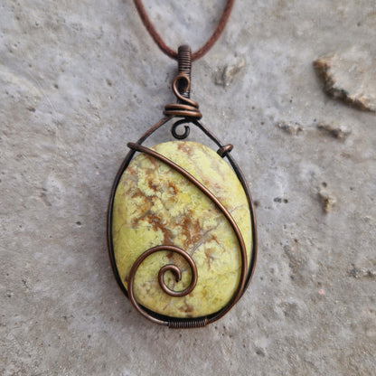 A close-up of a Green Opal wire wrapped pendant on a wax cord, for healing from grief